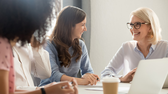 Four women sitting at a table with a laptop